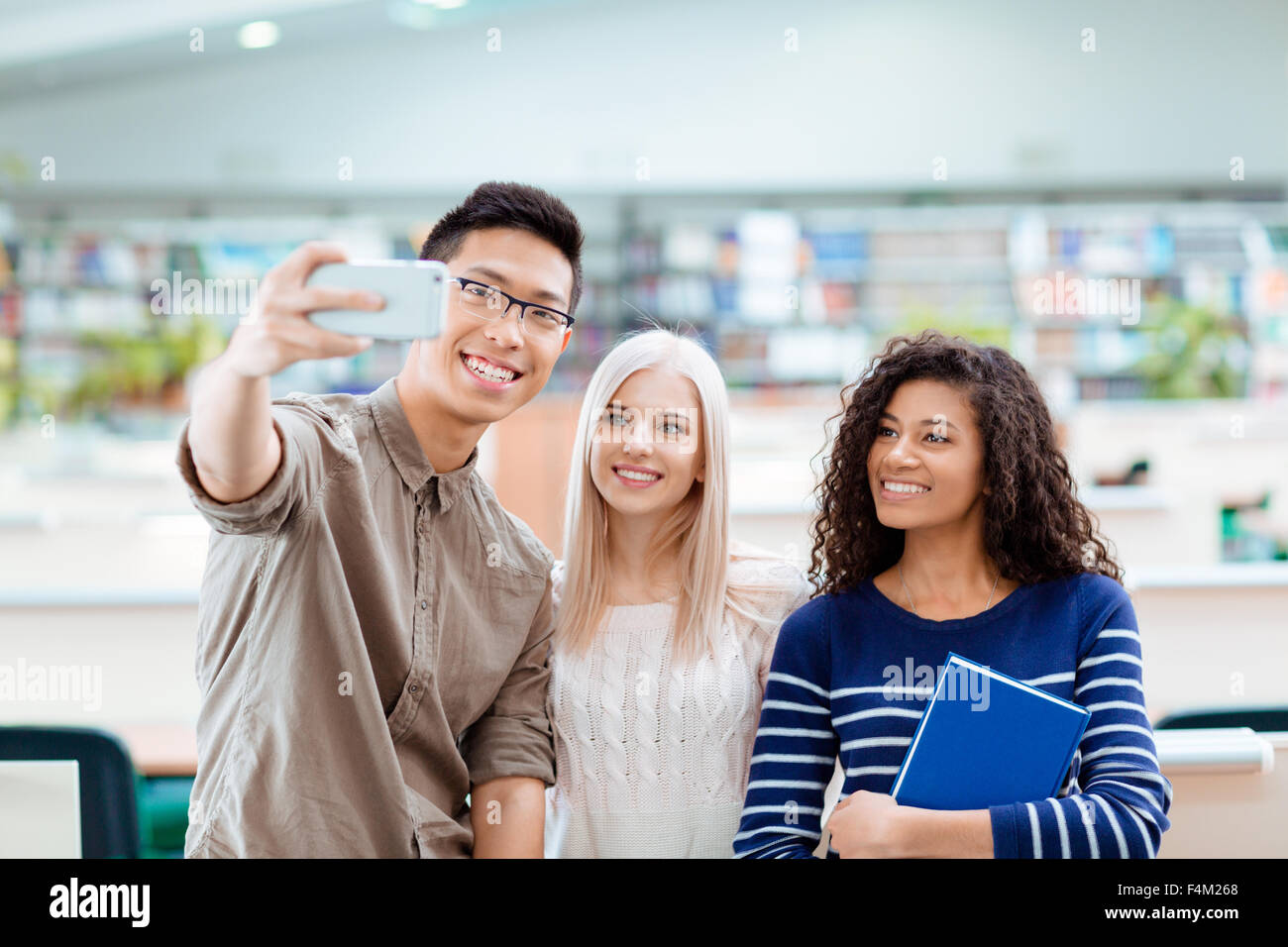Smiling multi ethnic students making selfie photo on smartphone in the university library Stock Photo