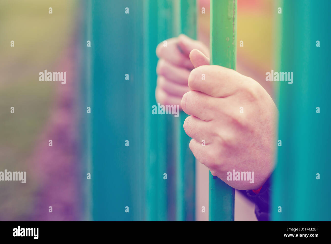Person behind bars, female hands gripping steel bars, concept of captivity and imprisonment, retro toned, selective focus Stock Photo