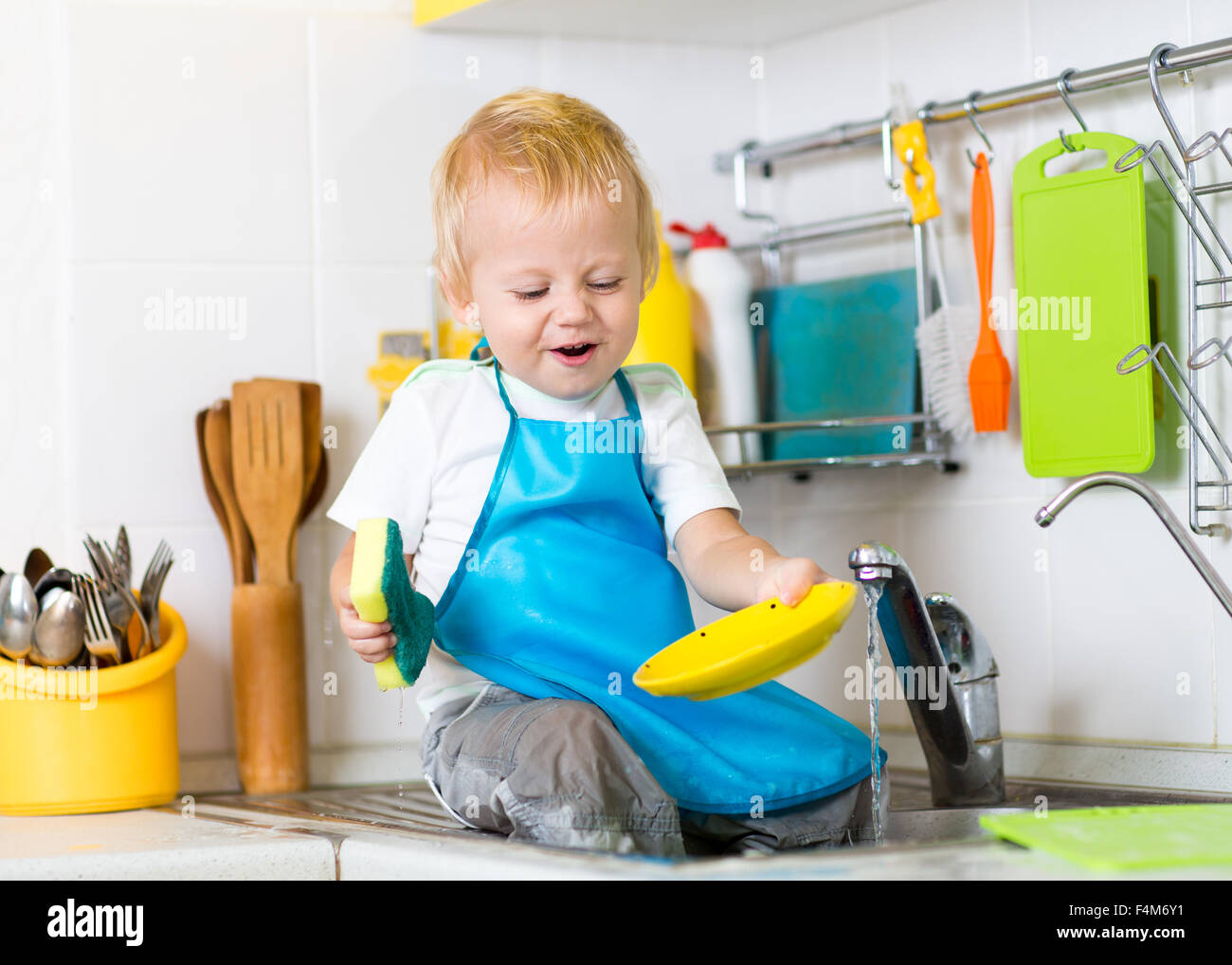Kid boy washing dishes and having fun in the kitchen Stock Photo