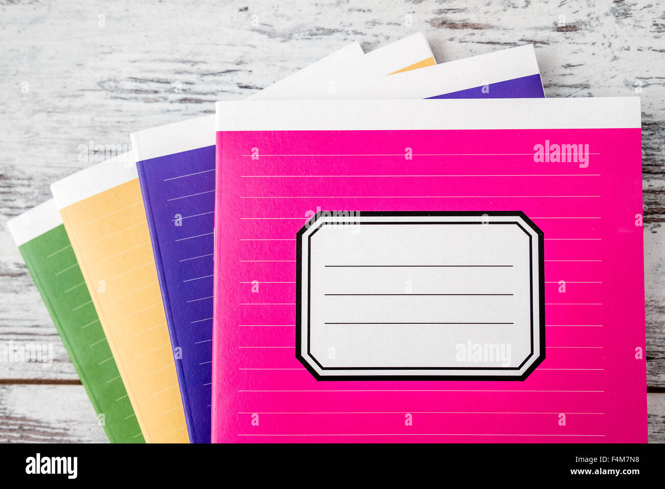 Colorful notebooks with name label on cover on white wooden background