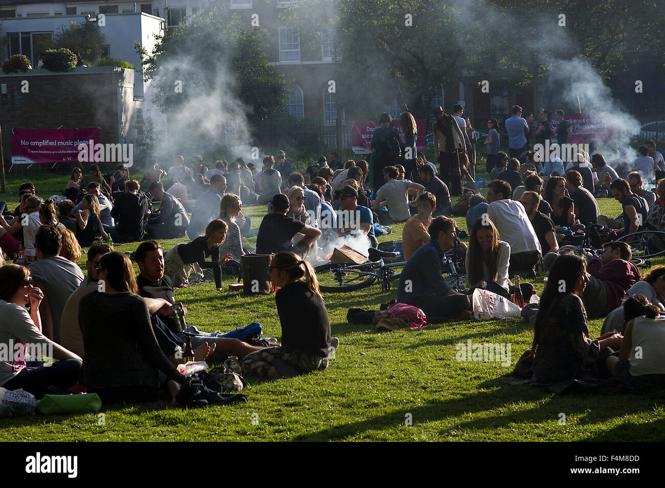 Large group of people in London Fields park on a sunny day, sitting on the grass, barbecuing, clouds of smoke rising Stock Photo