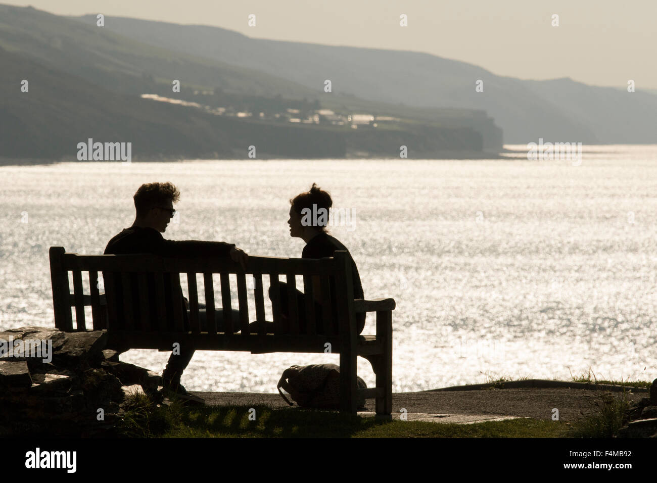 A young couple talk on a bench while overlooking the British coastline, Britain, UK Stock Photo