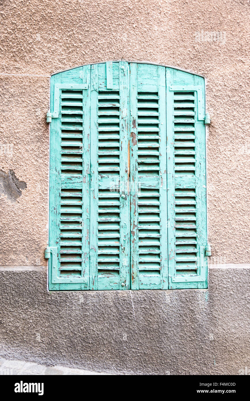 A shuttered window painted green on a rendered wall. With peeling paint