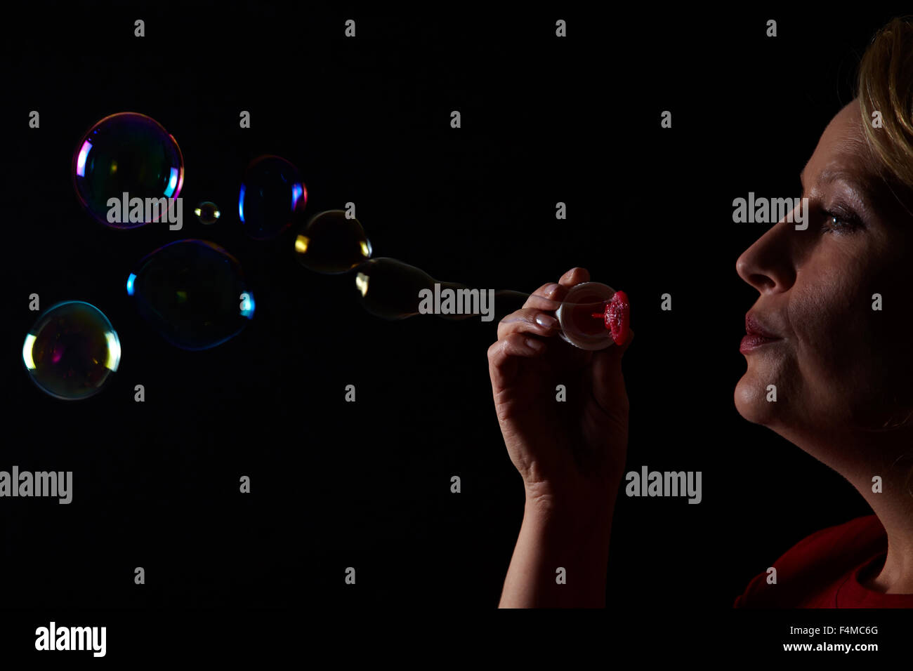 Woman blowing soap bubbles on black background Stock Photo