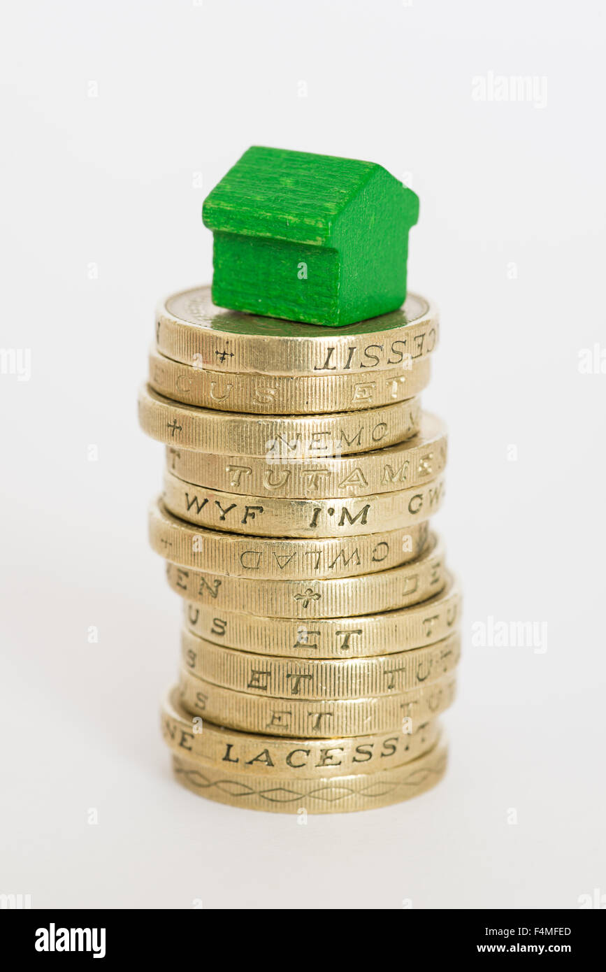 Stack of British one pound coins with a wooden Monopoly-style house sitting on top Stock Photo