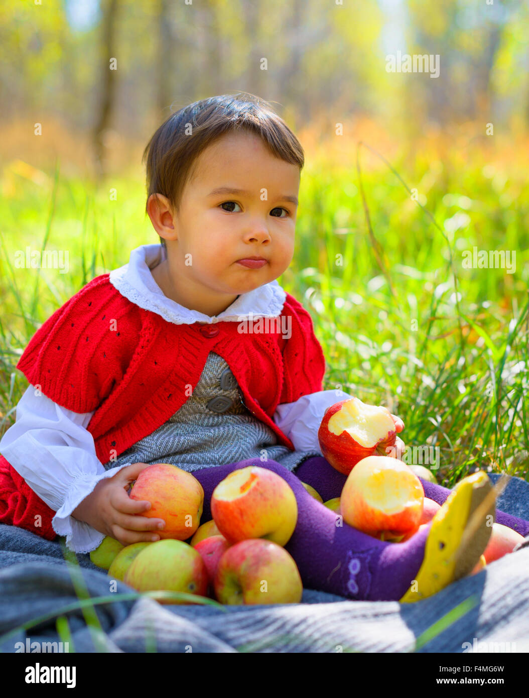 child with red apples sitting on leaves in autumn park Stock Photo