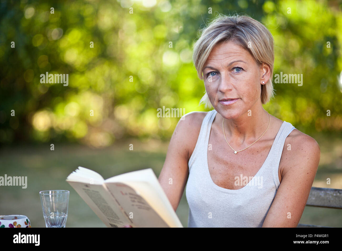 Cute woman reading a book outdoor sitting on a garden chair Stock Photo ...