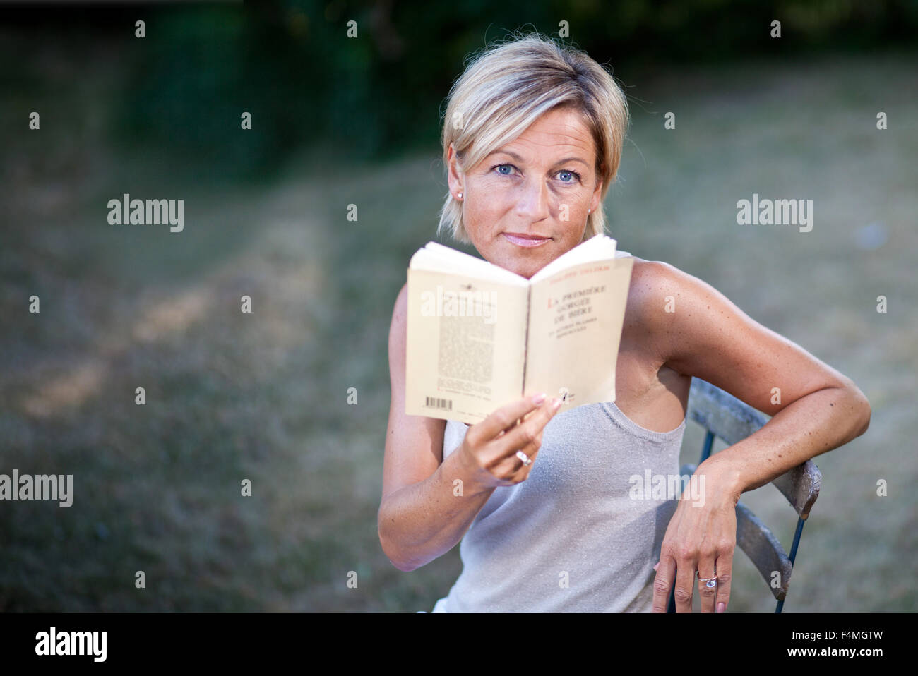 Cute woman reading a book outdoor sitting on a garden chair Stock Photo ...