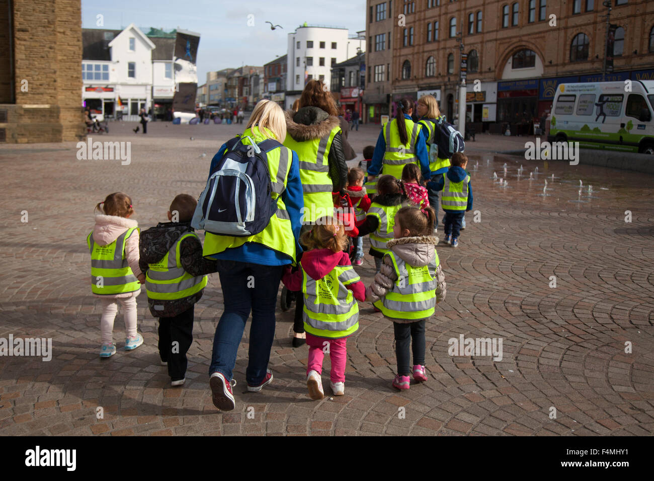 Safeguarding Pre-School primary; Children wearing protective fluorescent hi-vis hazard jackets on a walk around Blackpool with carers, Lancashire, UK Stock Photo