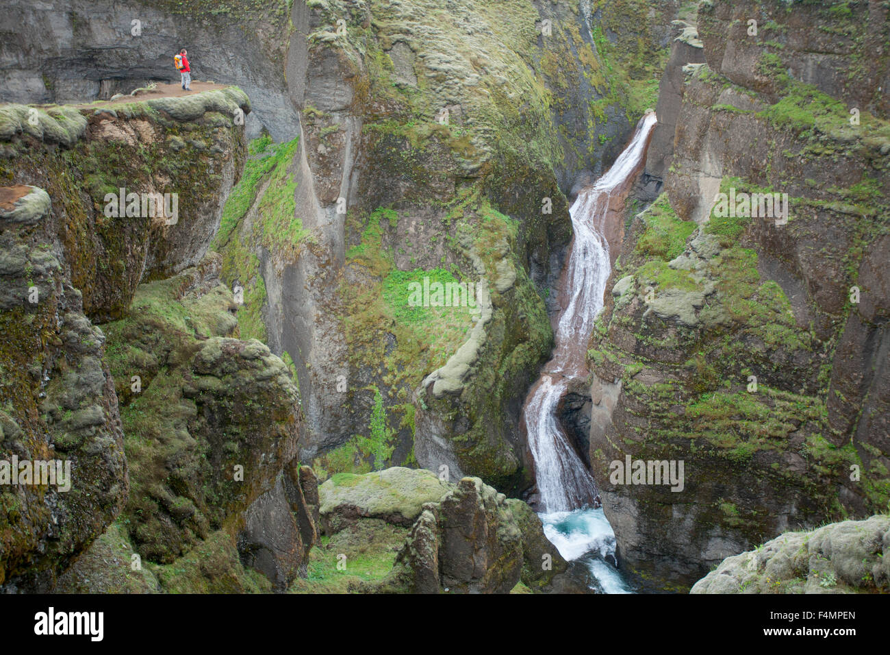Person dwarfed by a waterfall in the Fjadrargljufur Canyon, Sudhurland, Iceland. Stock Photo