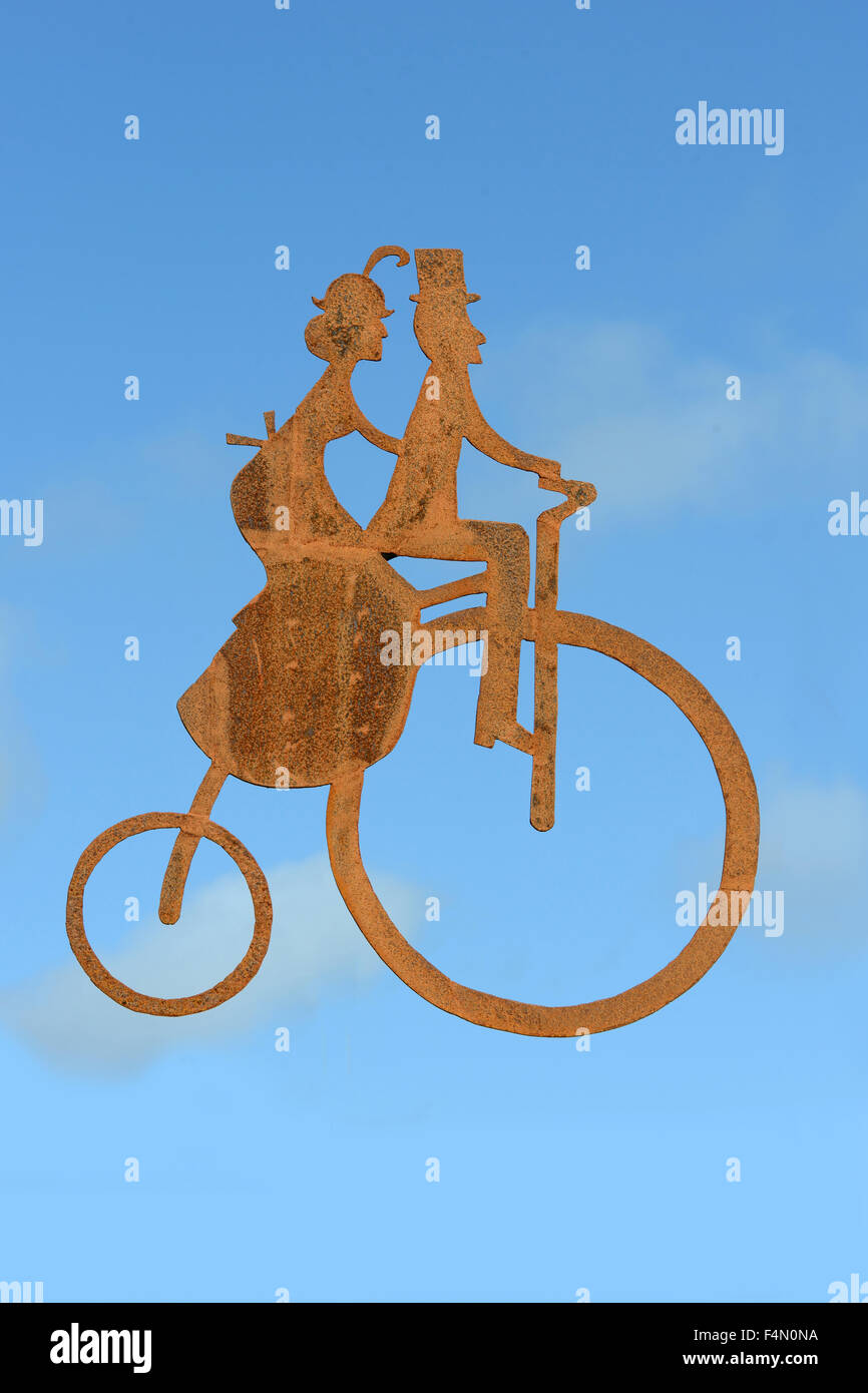 Rusty silhouette of a man and woman riding a penny farthing bicycle against a  blue sky Stock Photo