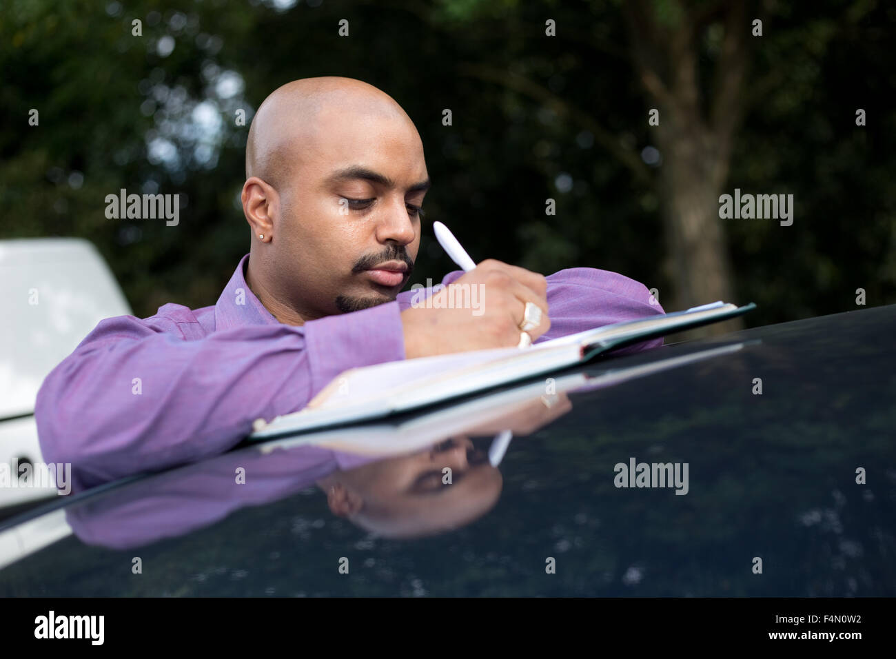 man writing notes leaning on his car roof Stock Photo
