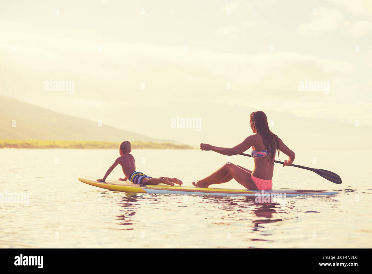 Mother and son stand up paddling at sunrise, Summer fun outdoor lifestyle Stock Photo