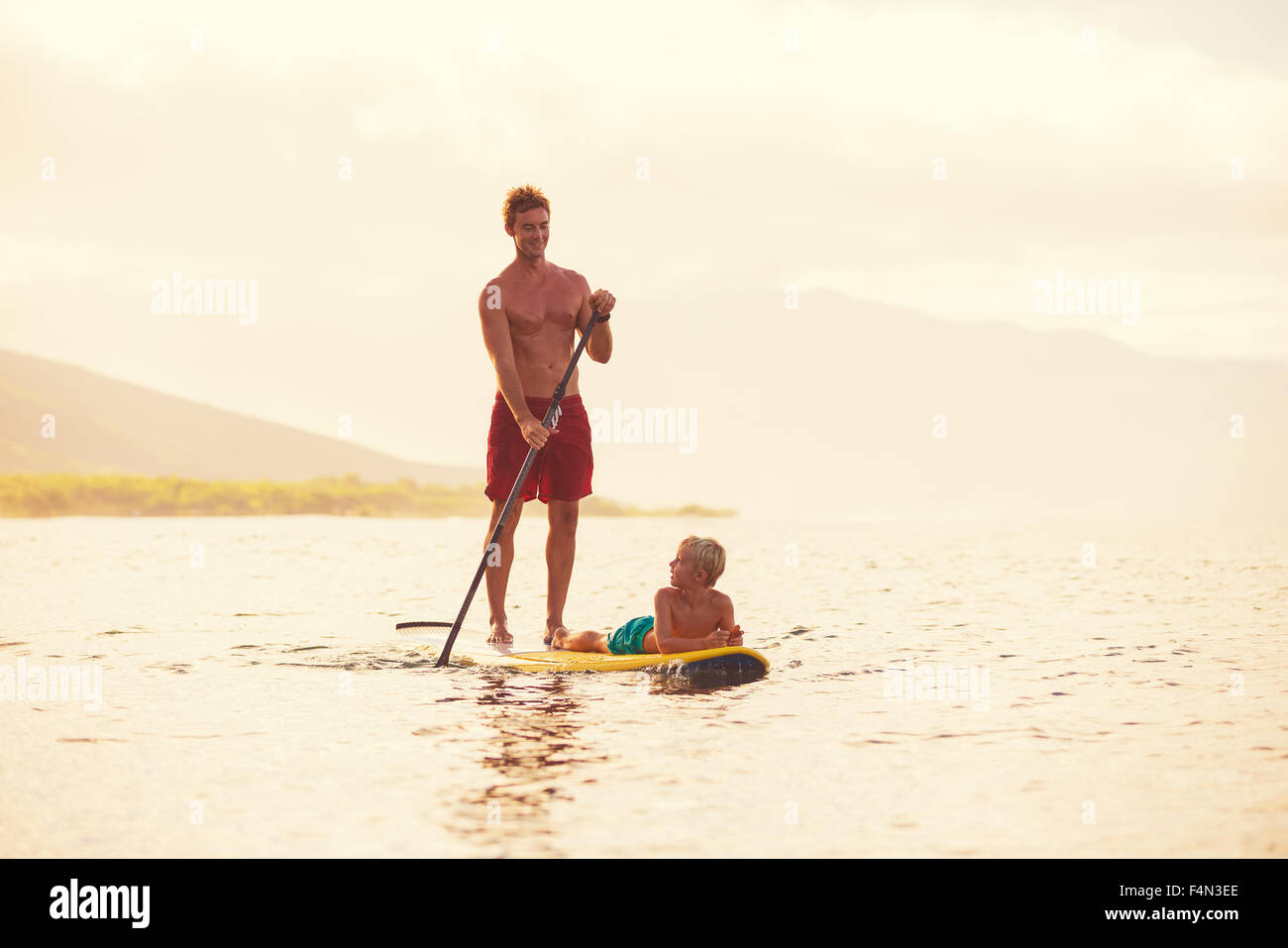 Father and son stand up paddling at sunrise, Summer fun outdoor lifestyle Stock Photo
