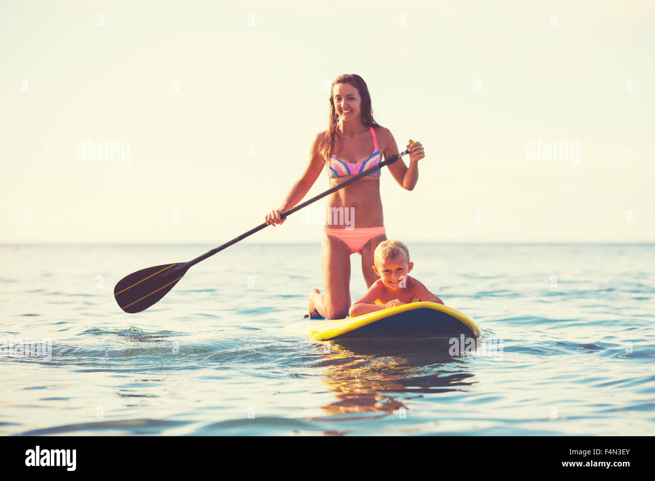 Mother and son stand up paddling at sunrise, Summer fun outdoor lifestyle Stock Photo