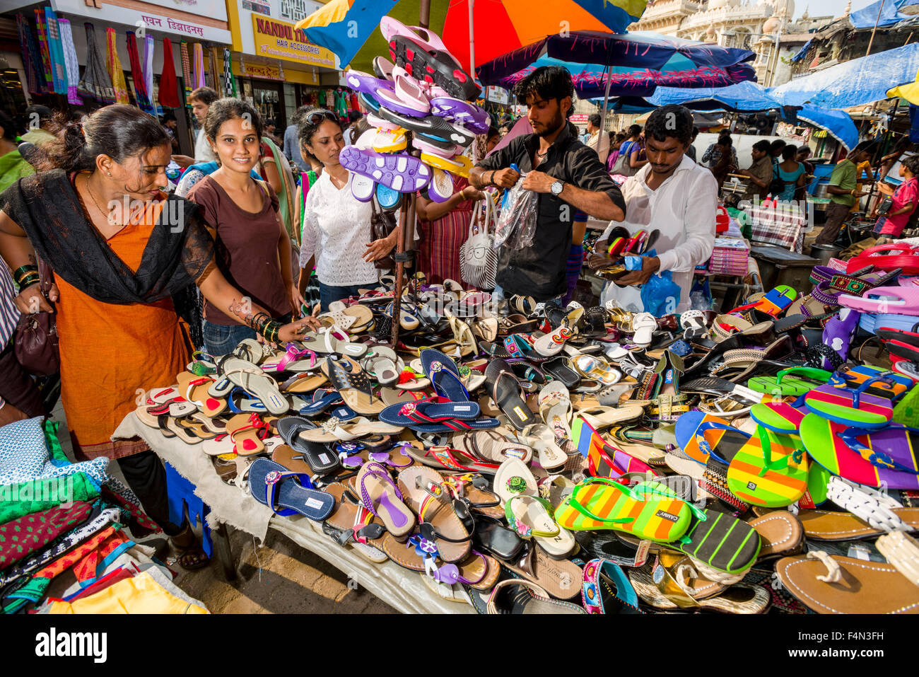 Salesmen are offering shoes for sale in a crowded street with shops at Mangaldas Market Stock Photo