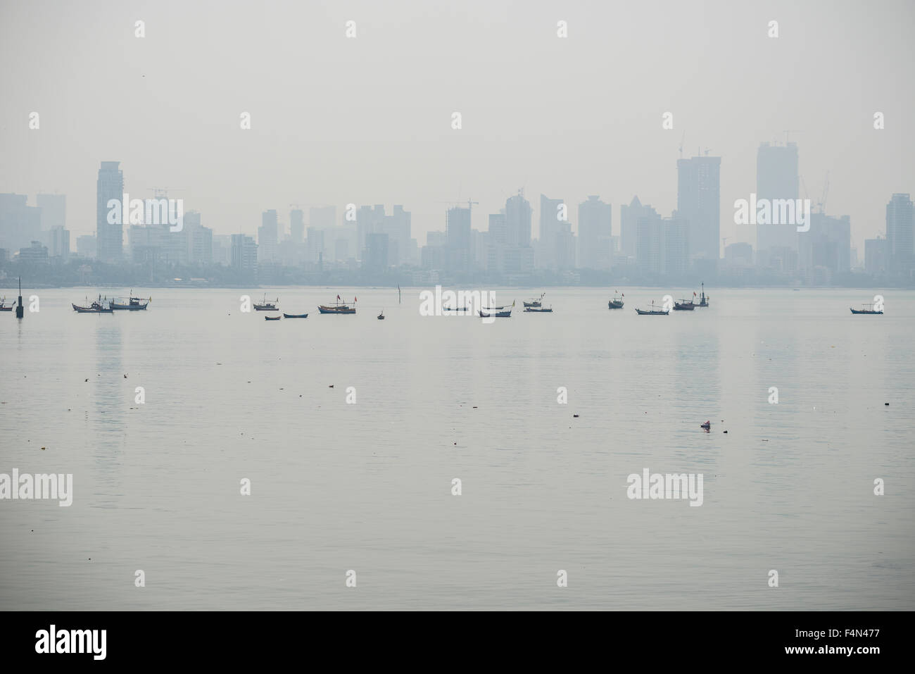 The skyline of the suburb Worli seen across the Mahim Bay with some fishing boats in the morning haze Stock Photo