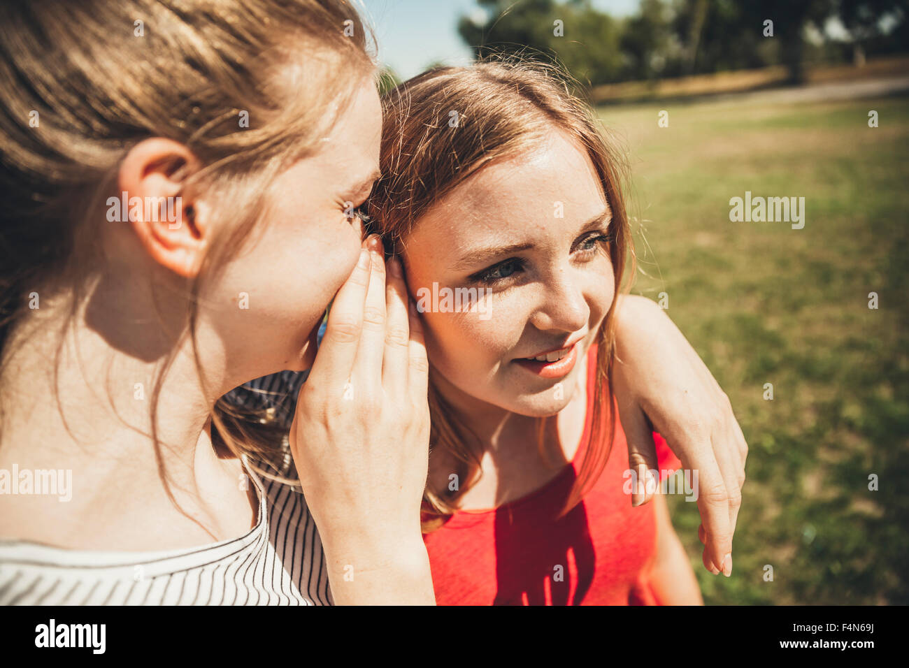 Two teenage girls whispering in park Stock Photo - Alamy