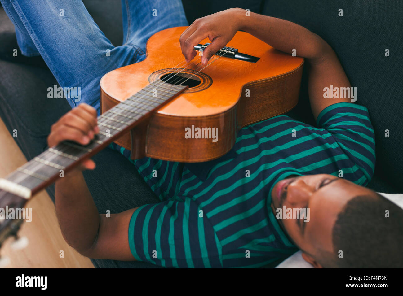 Man sitting on a couch playing guitar Stock Photo - Alamy