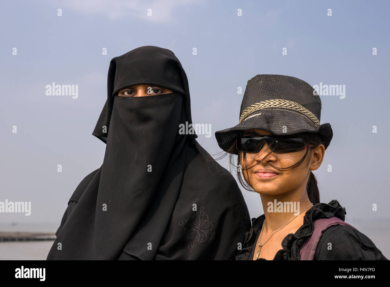 A portrait of two muslim women in contrast to each other, one dressed in the traditional black burka, hijab, and the other one i Stock Photo