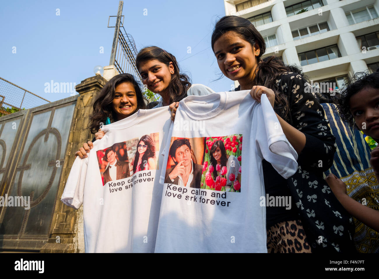 Three young women are displaying t-shirts with portraits of the actor Shahrukh Khan at the gate of his villa at his birthday in Stock Photo