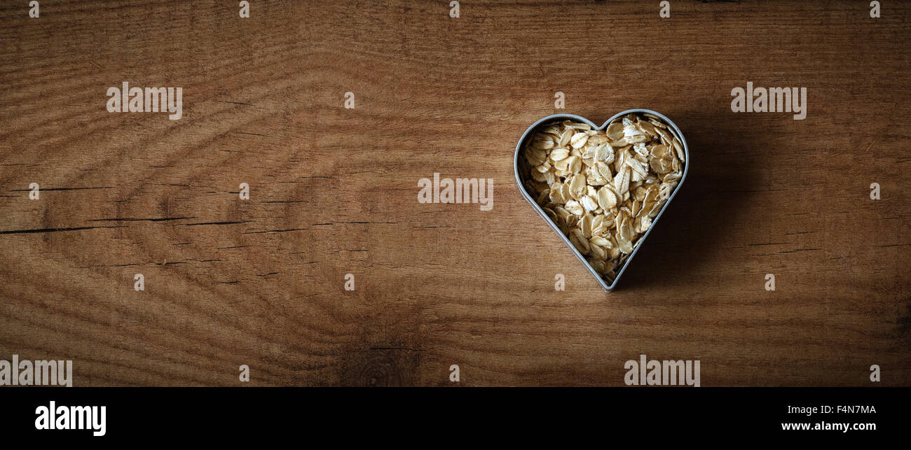 Rolled oats in a heart-shaped cookie cutter on wood Stock Photo