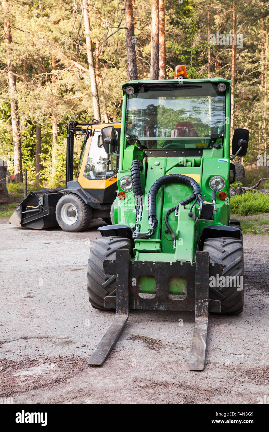 Green small forklift stands on a logging area in forest, vertical photo Stock Photo