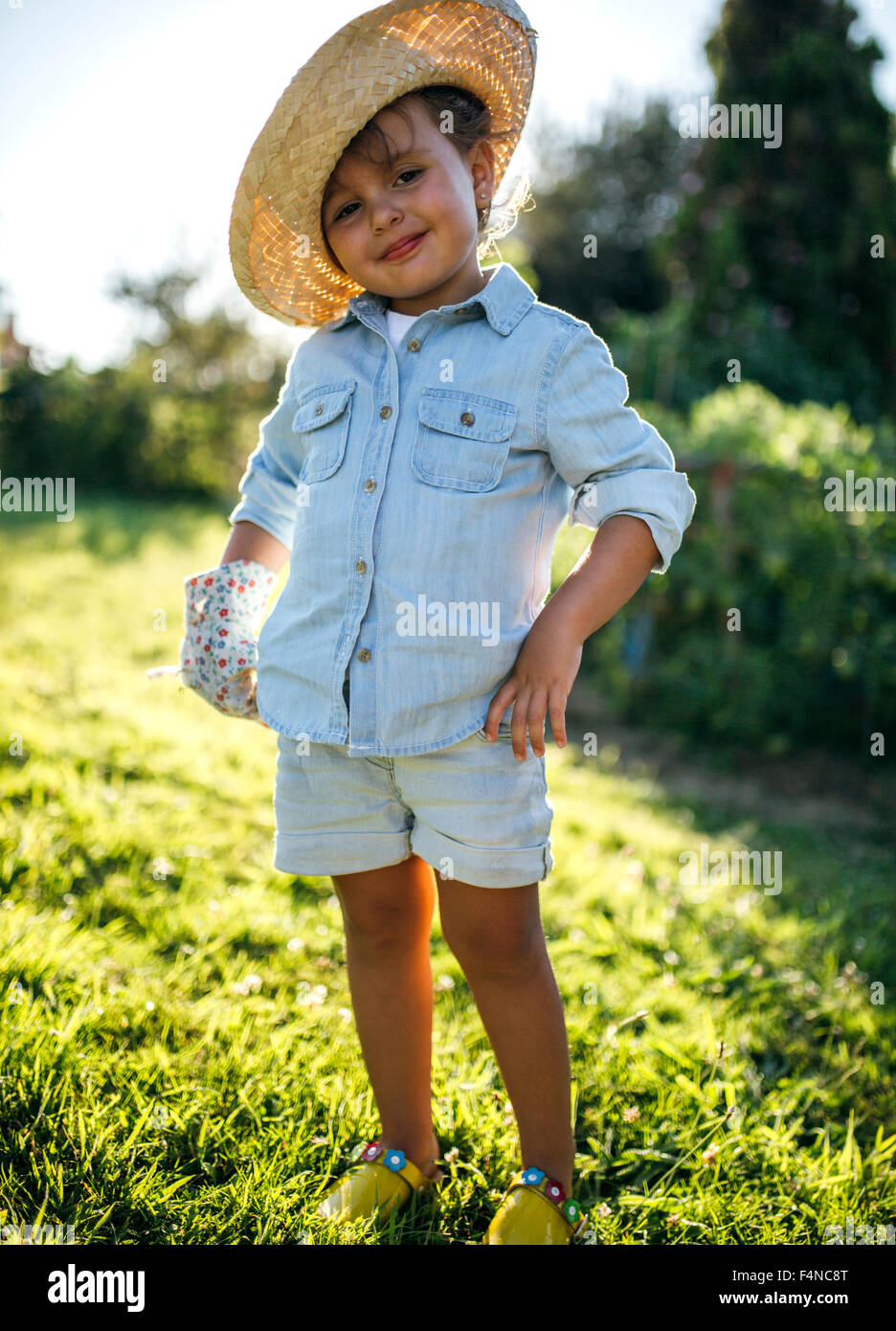 Portrait of smiling little girl wearing straw hat standing in a garden ...