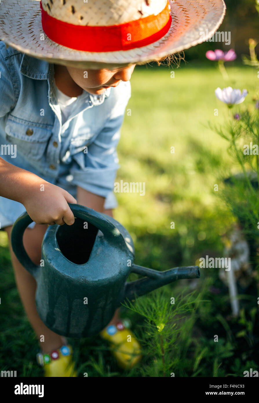 Little girl wearing straw hat watering flowers in the garden Stock