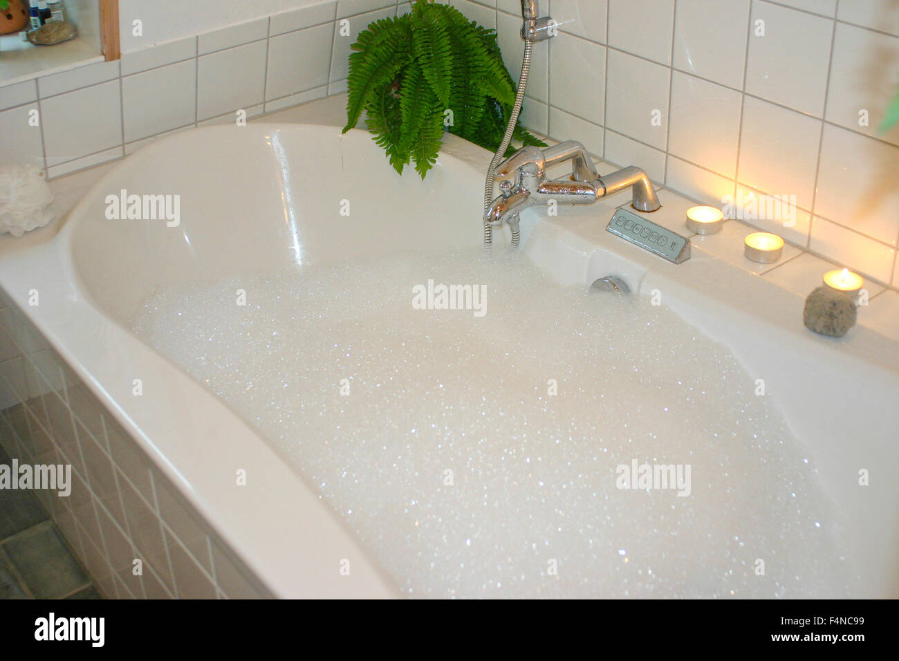 Bathtub with foamy water candles and a plant Stock Photo