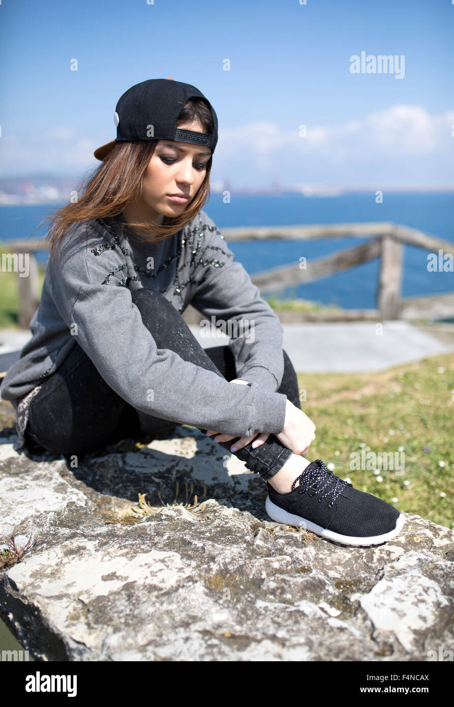 Spain, Gijon, portrait of young woman wearing baseball cap sitting on a