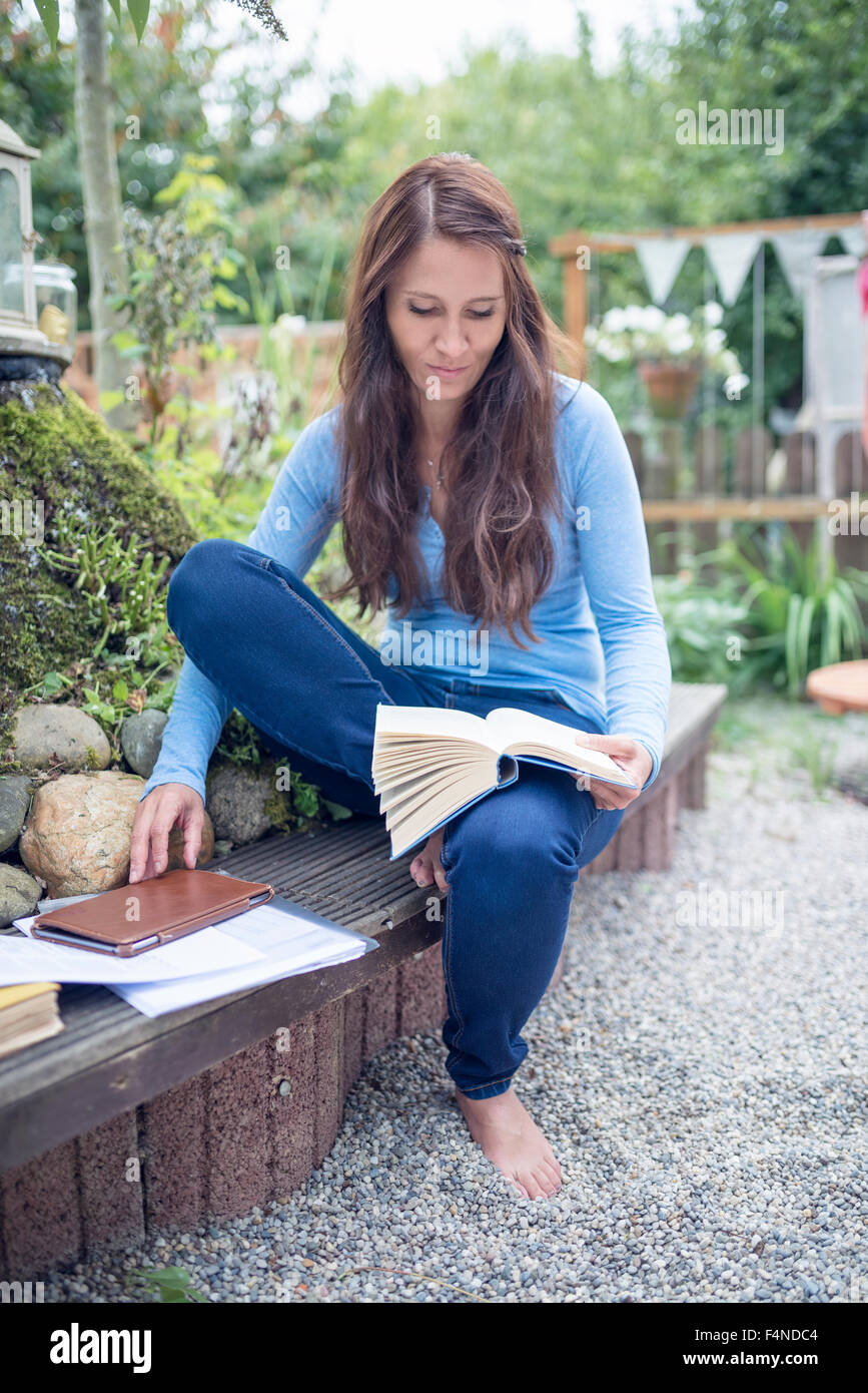 Woman sitting on a bench in the garden reading a book Stock Photo - Alamy