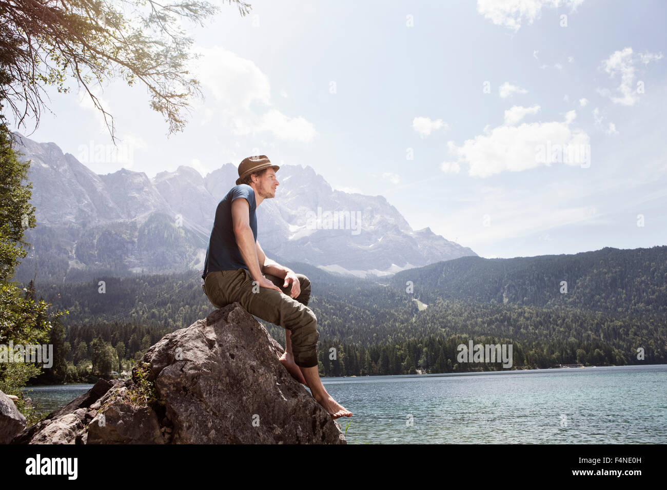 Germany, Bavaria, Eibsee, man sitting on rock on lakeshore Stock Photo