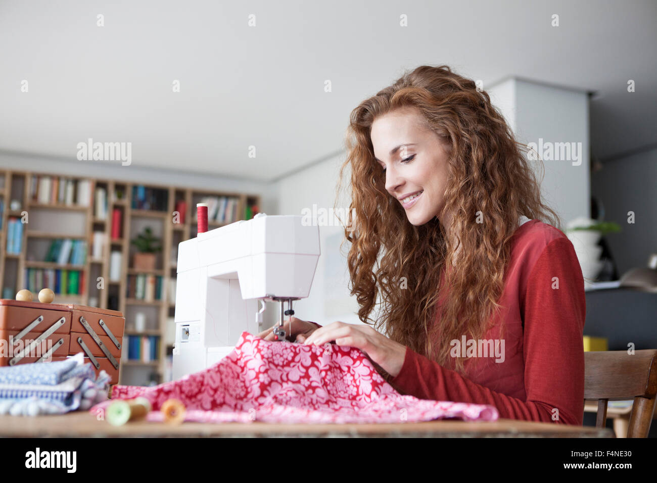 Smiling woman at home using sewing machine Stock Photo