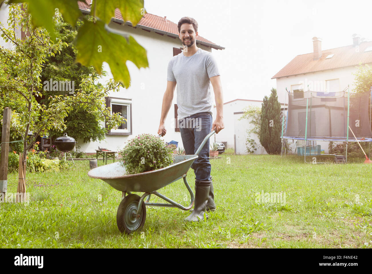 Man pushing wheelbarrow with plant in garden Stock Photo