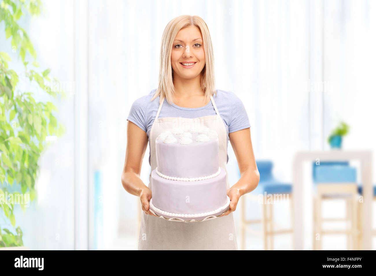 Young blond housewife holding a large cake and looking at the camera at home Stock Photo