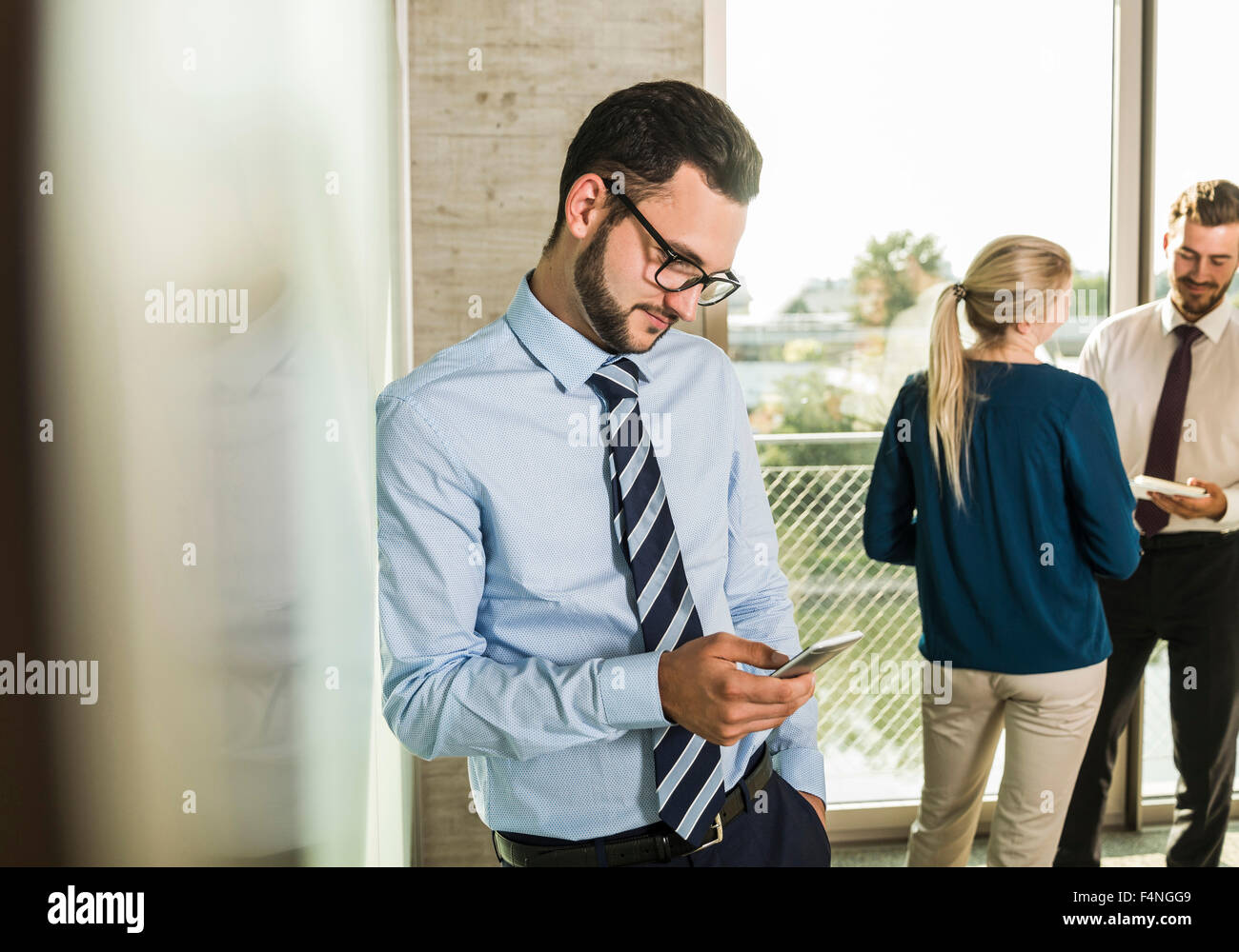 Businessman looking at smartphone with colleagues in background Stock Photo
