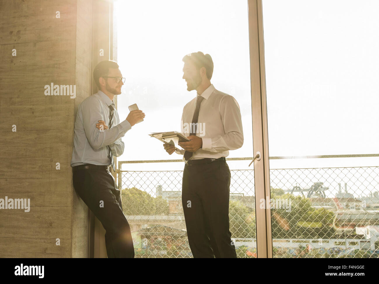 Two young businessmen talking at the window in office Stock Photo - Alamy