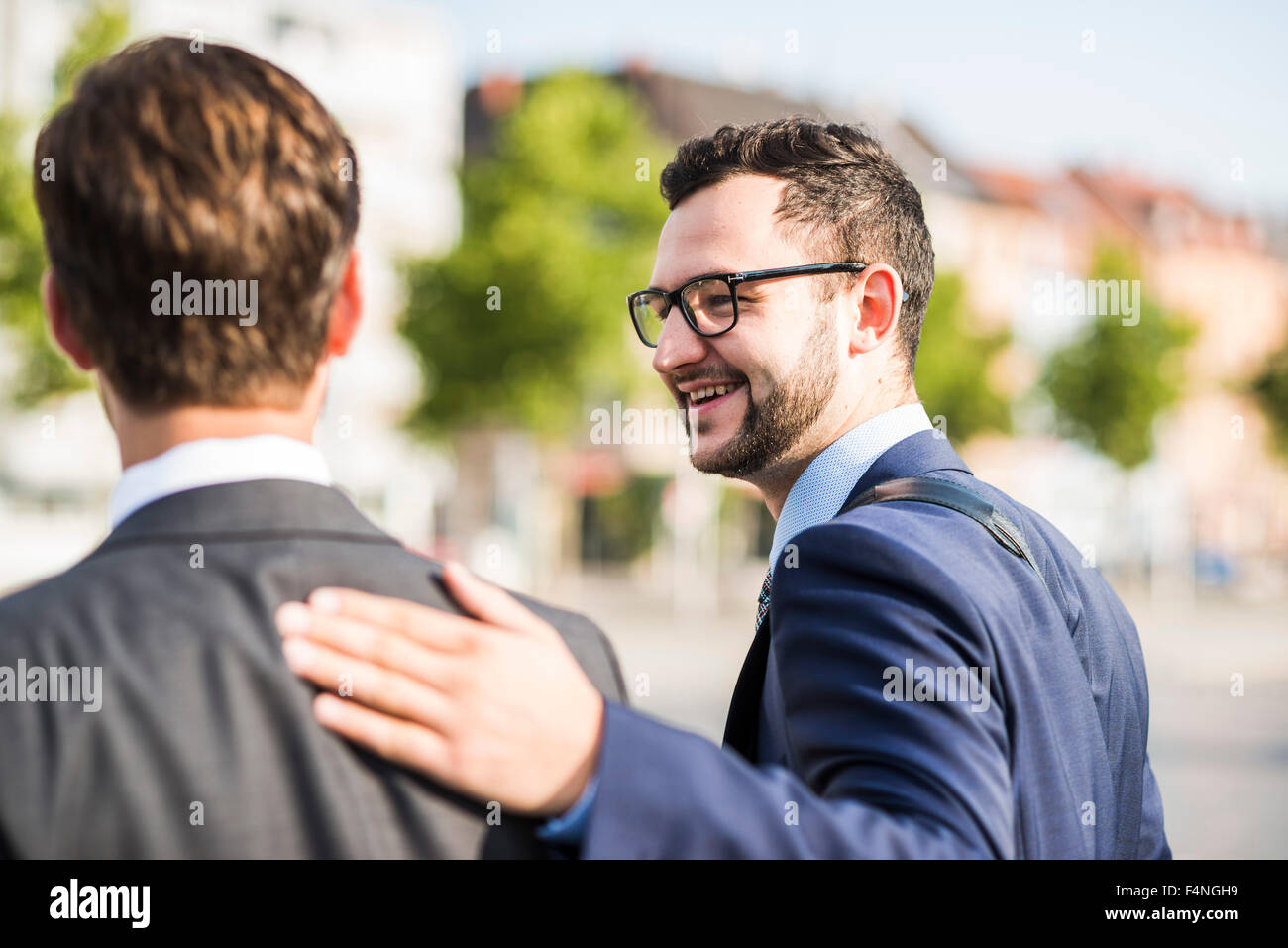 Two young businessmen walking in city, one patting colleagues back Stock Photo