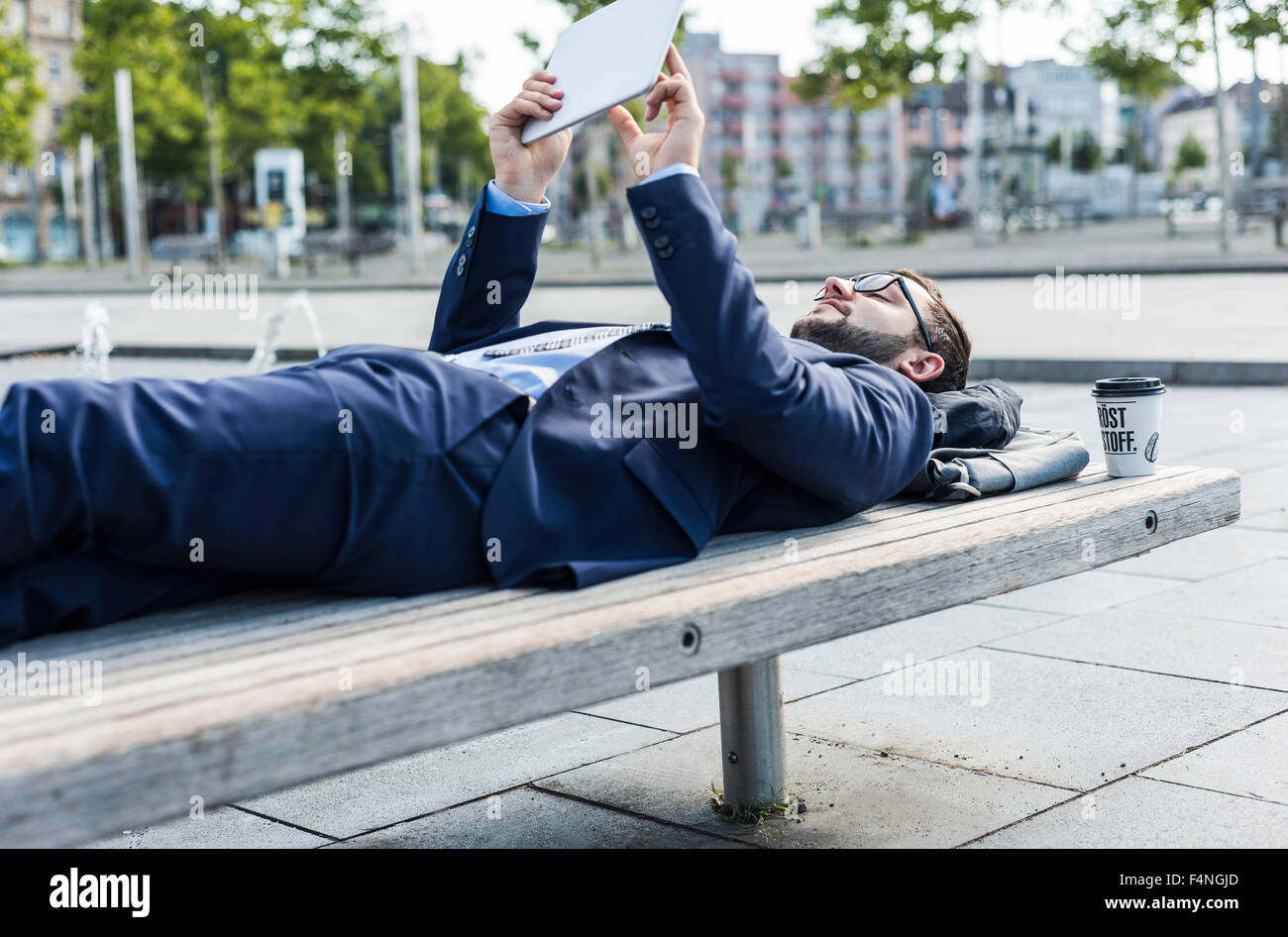 Young businessman lying on bench, working Stock Photo