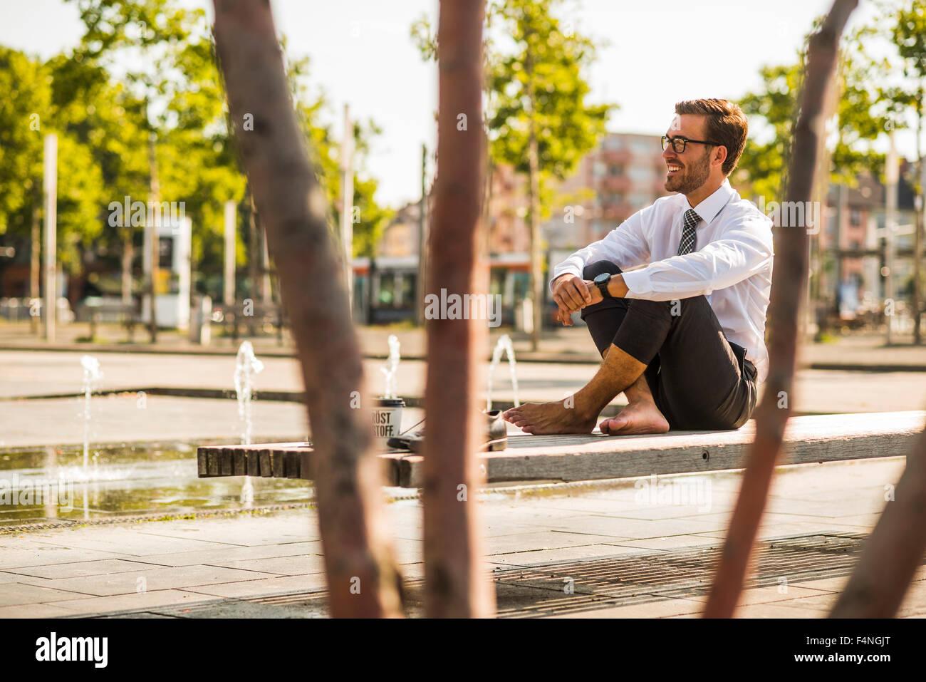 Young businessman sitting cross-legged on bench Stock Photo - Alamy