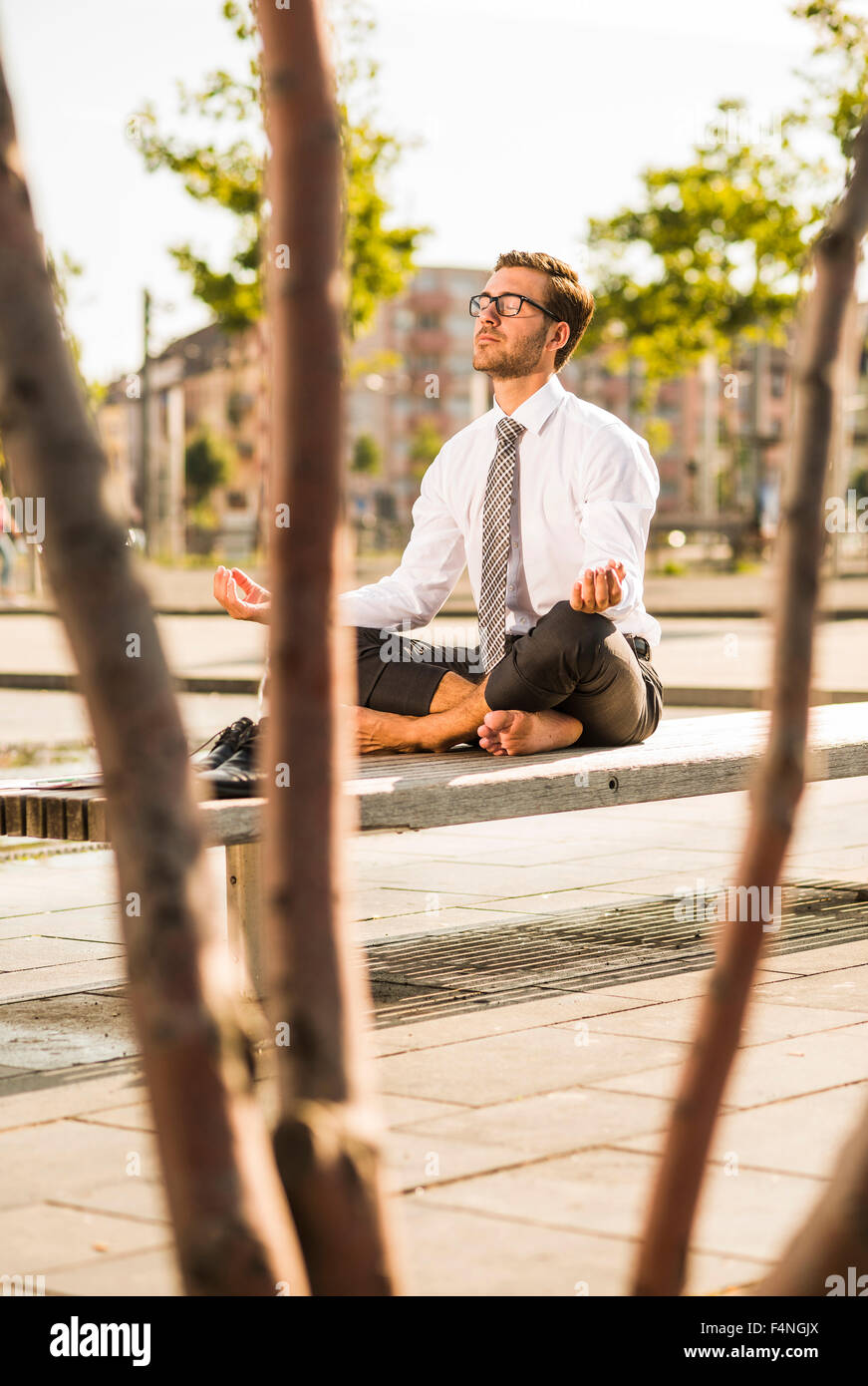 Young businessman meditating on bench Stock Photo