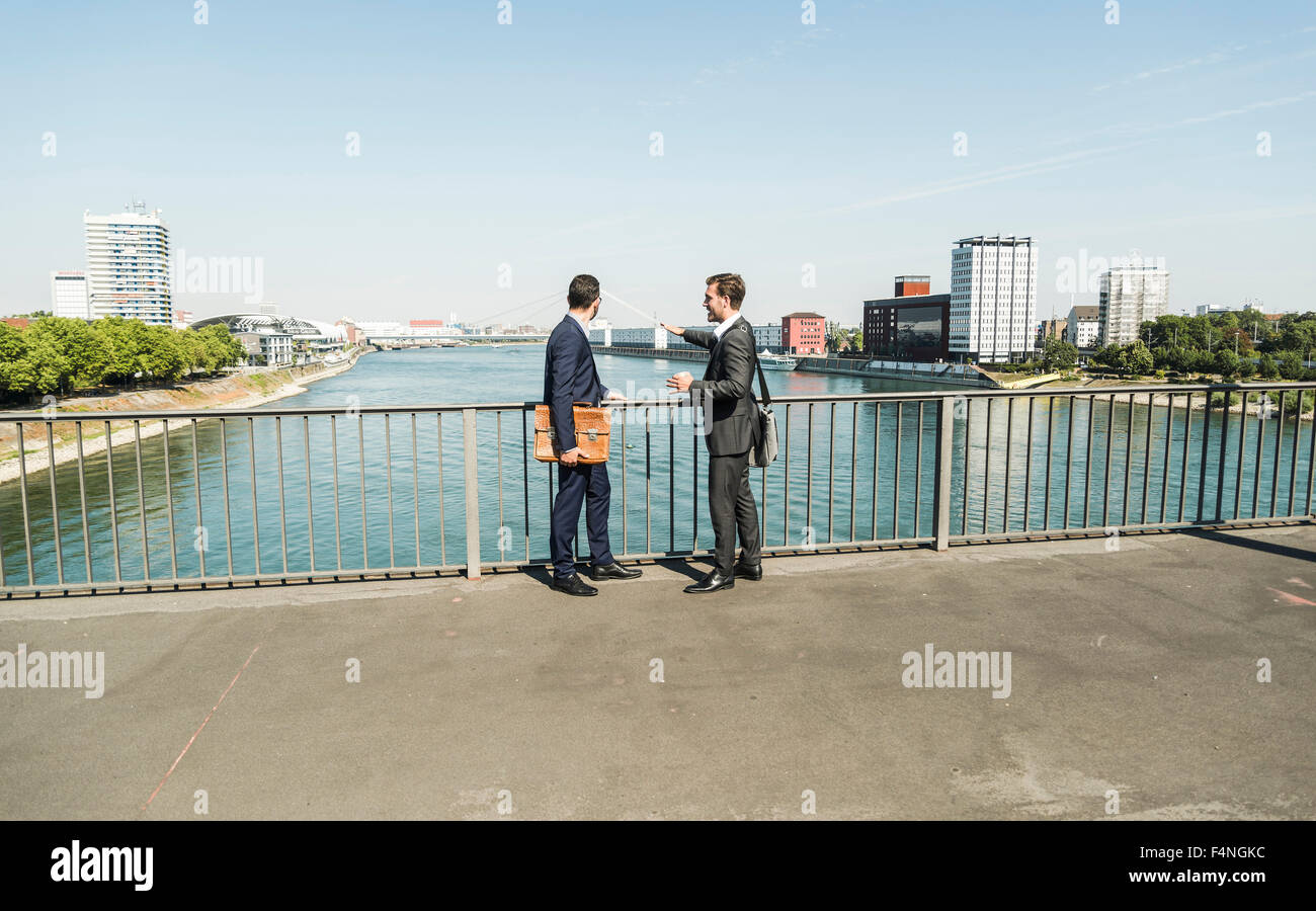 Young businessmen standing at railing looking at river Stock Photo