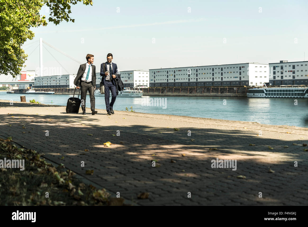 Two young businessmen on a business trip, walking by river Stock Photo