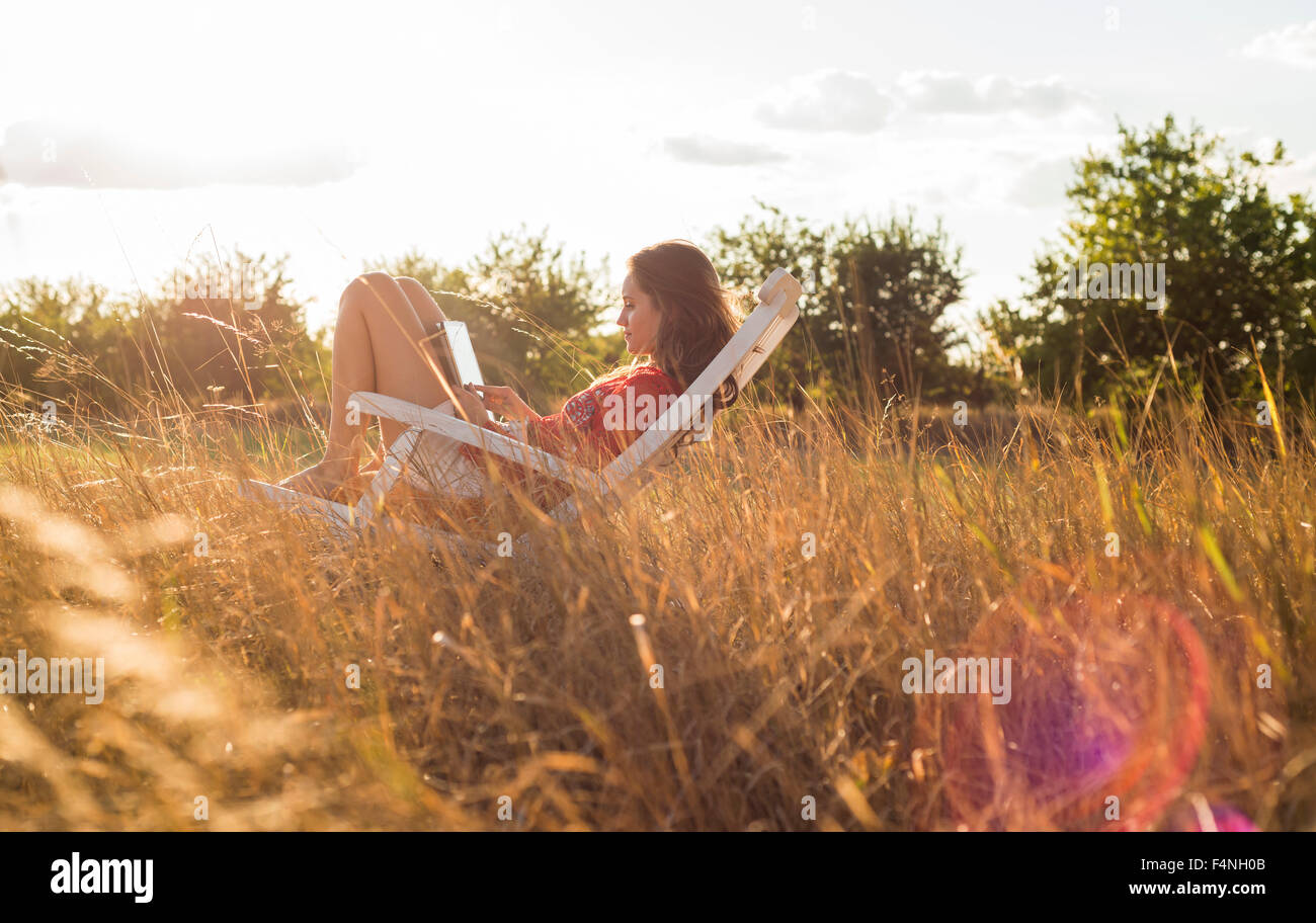 Woman sitting on a deck chair on a meadow using digital tablet Stock Photo