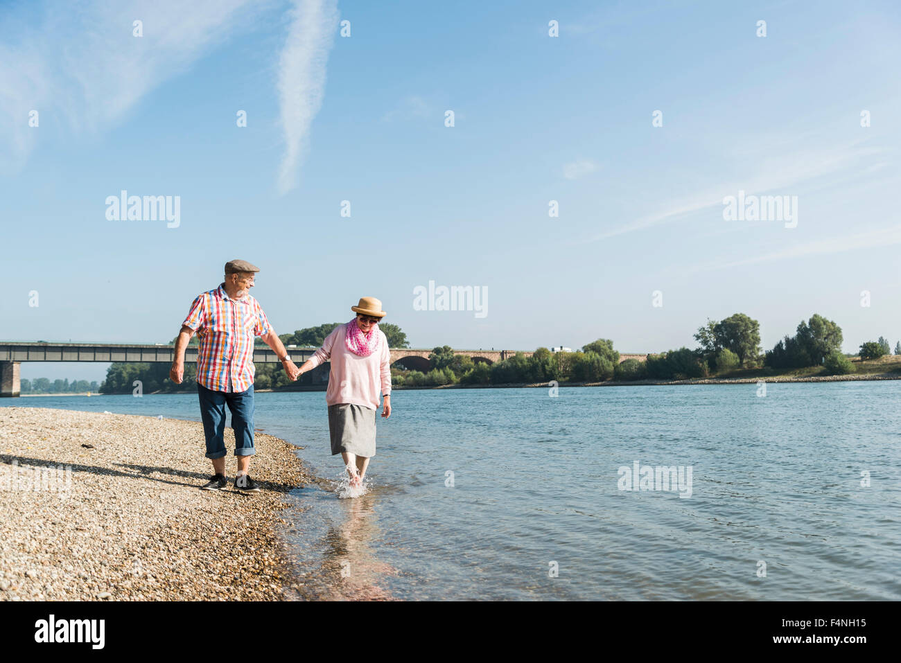 Germany, Ludwigshafen, happy senior couple walking hand in hand at riverside Stock Photo