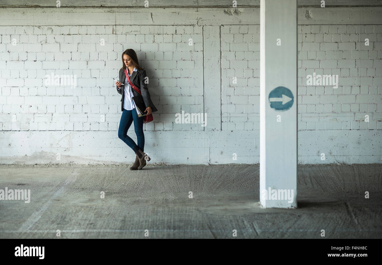 Young woman in a car park holding folder and looking at cell phone Stock Photo