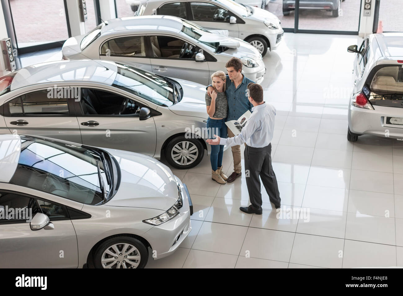 Car dealer showing new car to young couple in showroom Stock Photo
