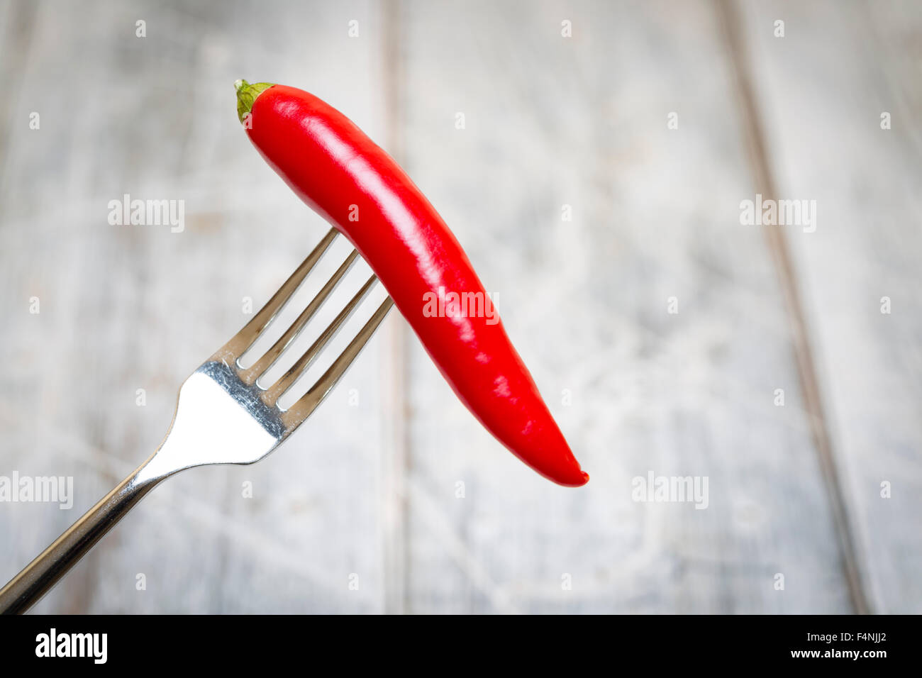 Red Chilli on fork over a rustic white blurred background Stock Photo