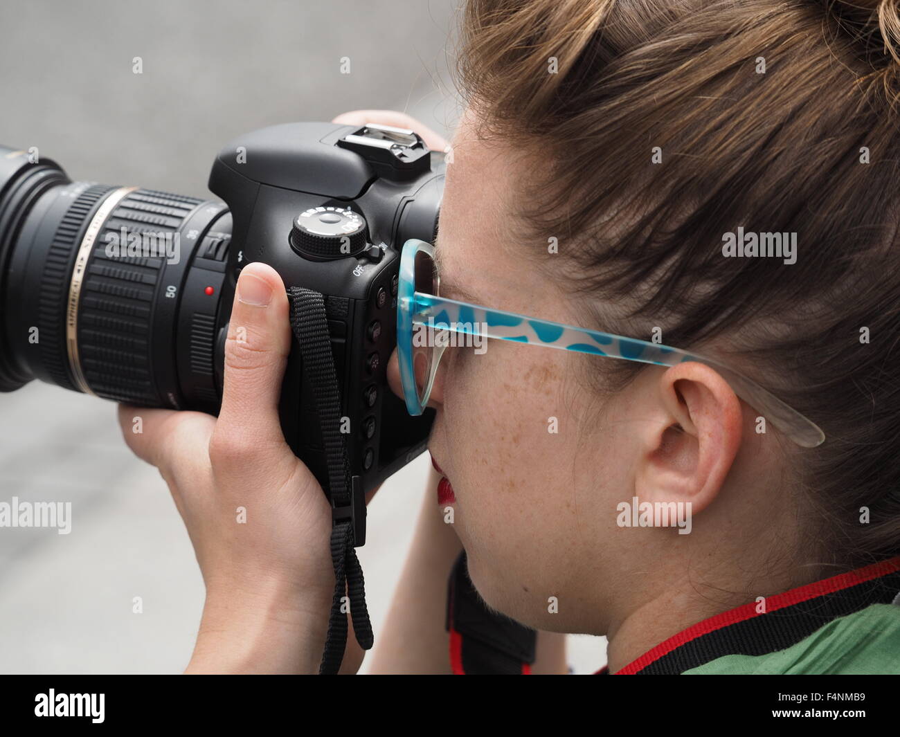 Female photographer wearing sunglasses looking through viewfinder of DSLR camera with zoom lens Stock Photo